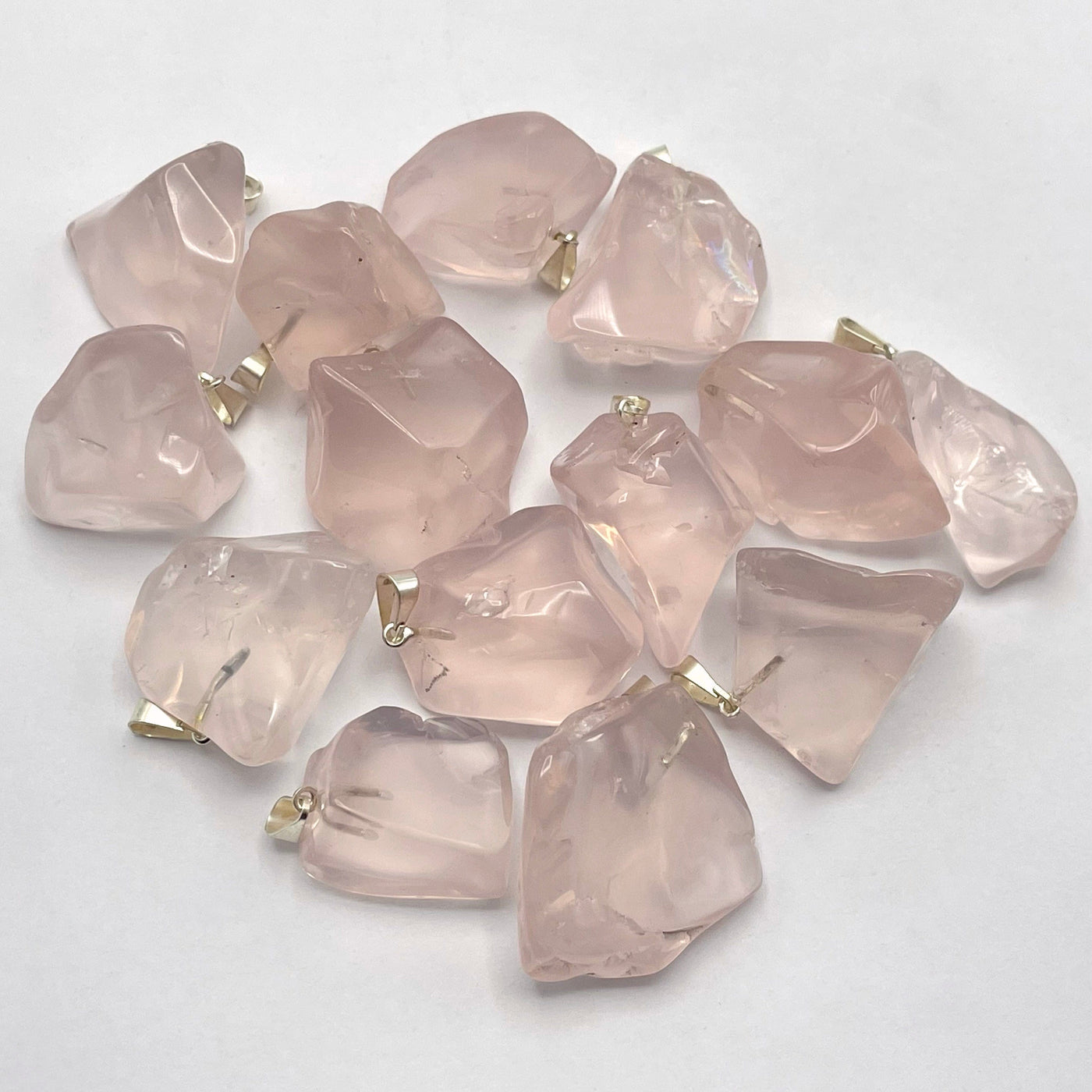 many tumbled rose quartz pendants in a pile on white background