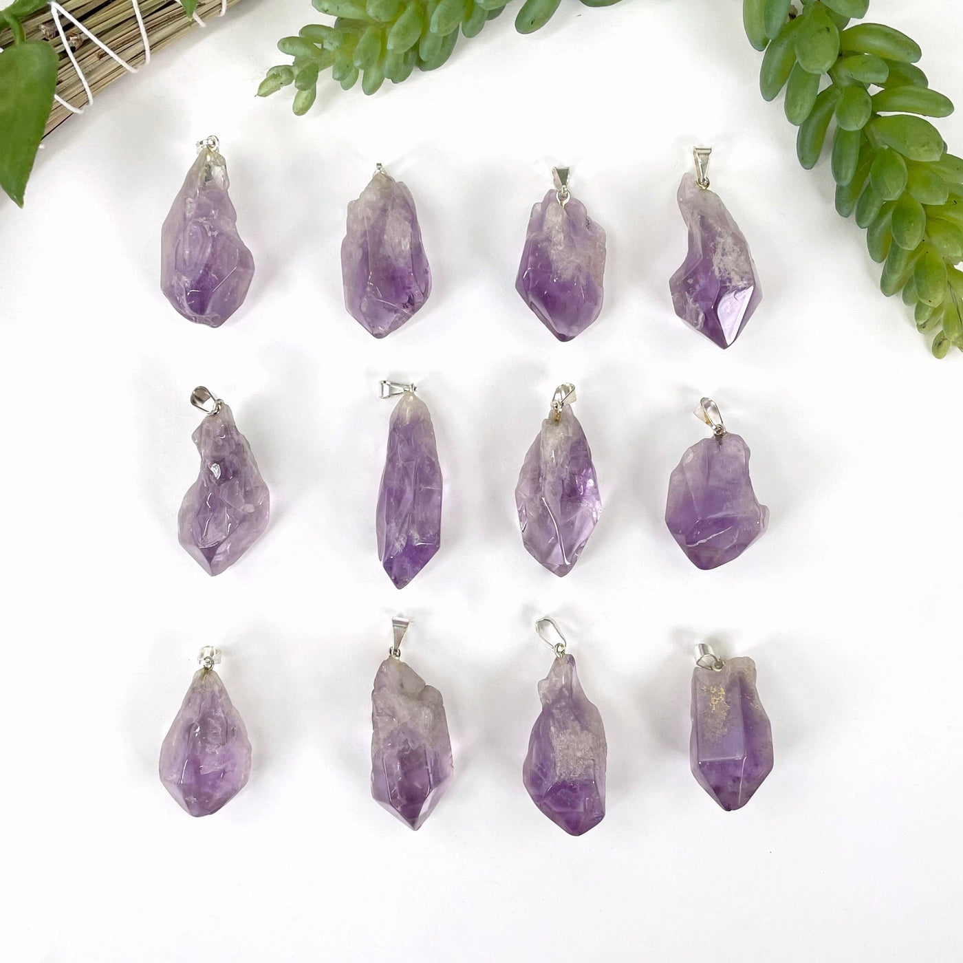 many tumbled amethyst pendants in three rows on white background for possible variations