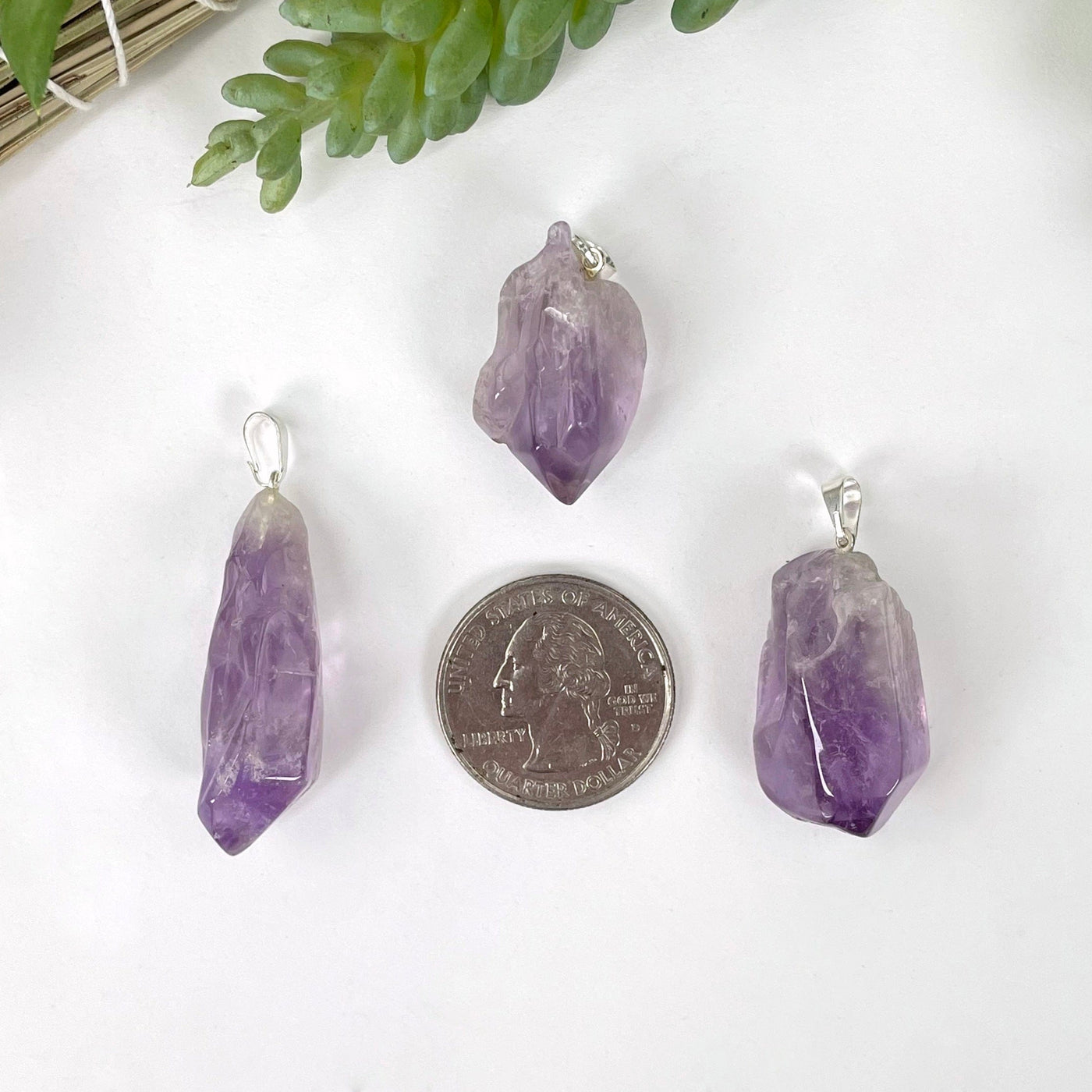 three tumbled amethyst pendants on white background with quarter for size reference