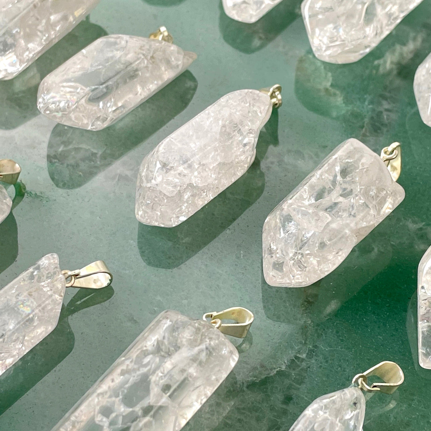 angled view of many crackle quartz point pendants on green background for thickness and details