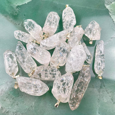 many crackle quartz point pendants in a pile on green background