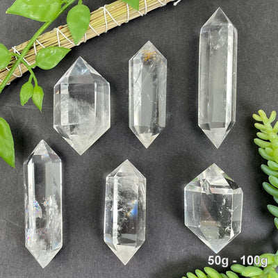 many 50g - 100g crystal quartz points on black background with plant decorations for possible variations