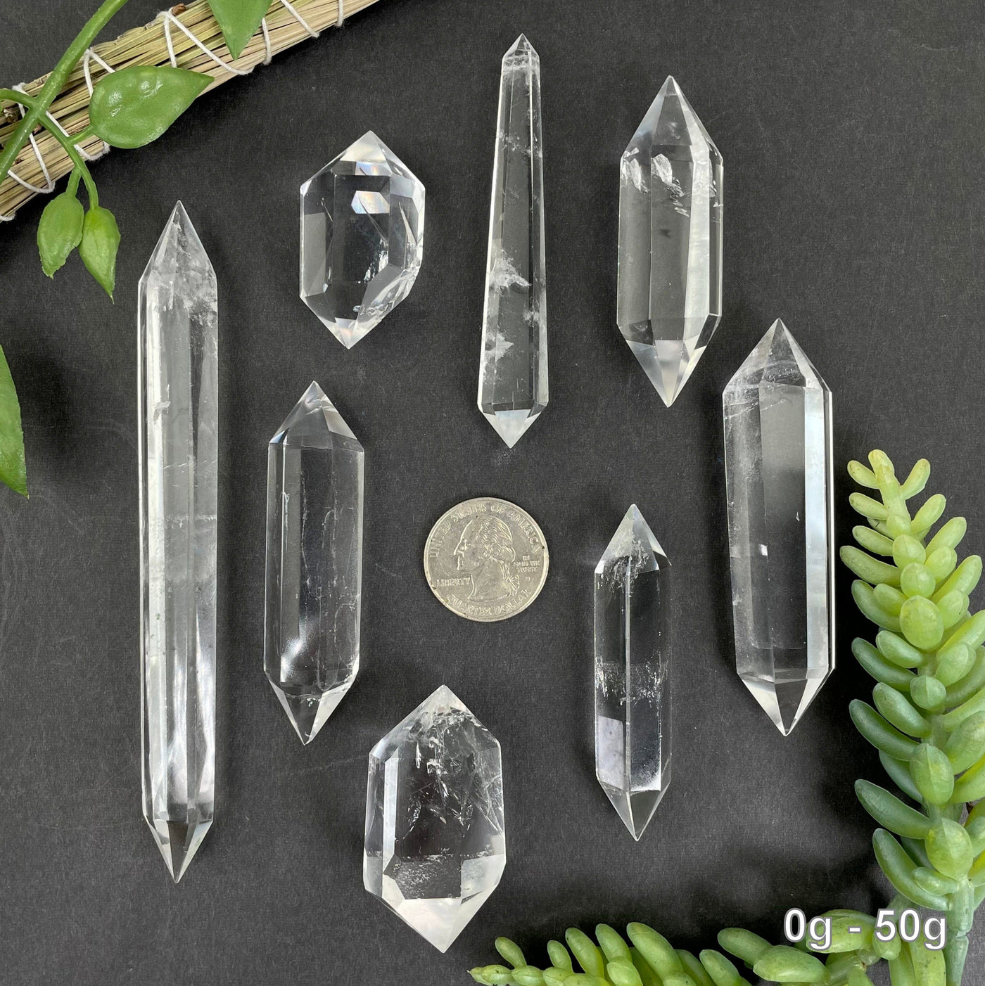 many 0g - 50g crystal quartz points on black background with quarter for size reference