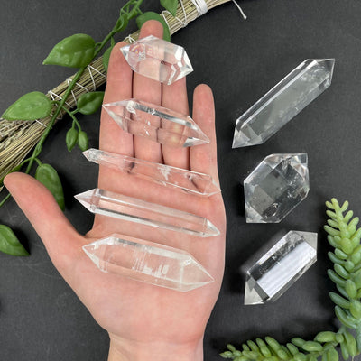 five 0g - 50g crystal quartz points in hand for size reference and possible variations with three 50g - 100g crystal quartz points on black backdrop