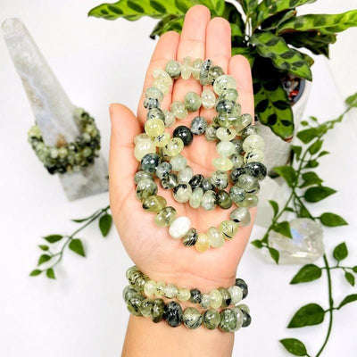 Group of prehnite bracelets in a woman's hand with plants and crystals in the background