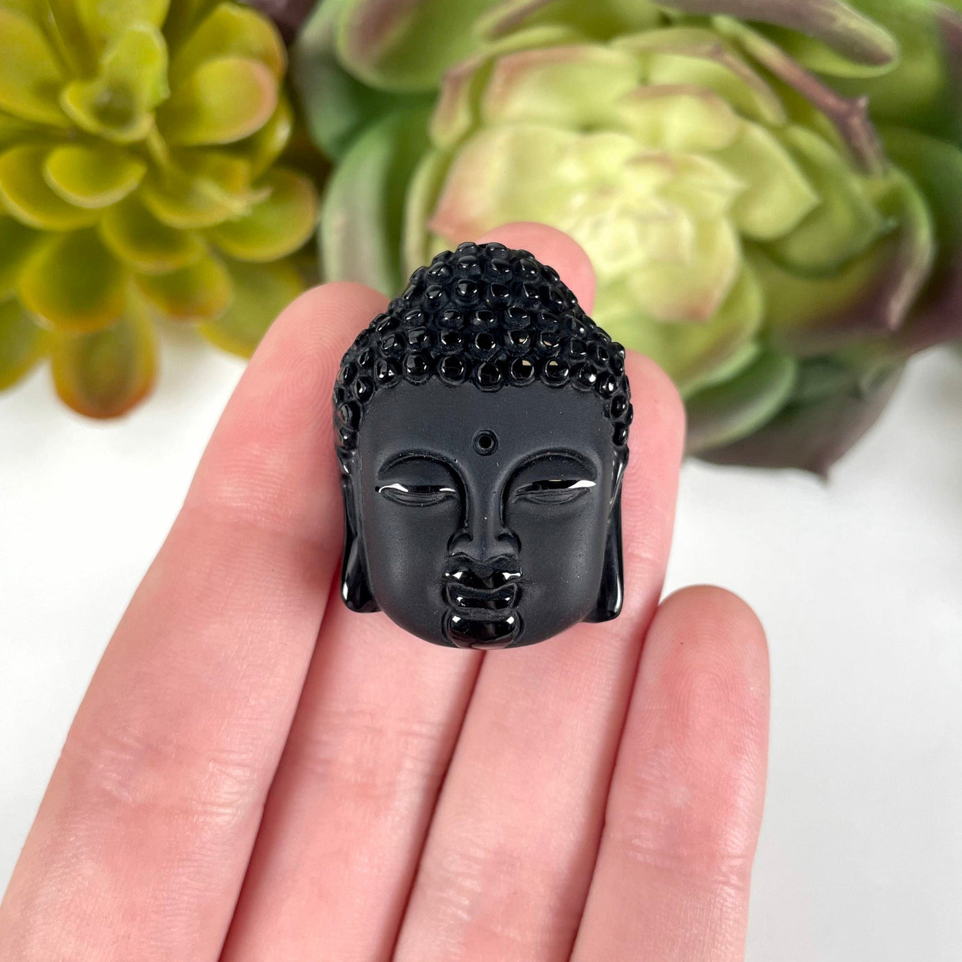 close up of one small black onyx buddha head bead in hand for size reference and details