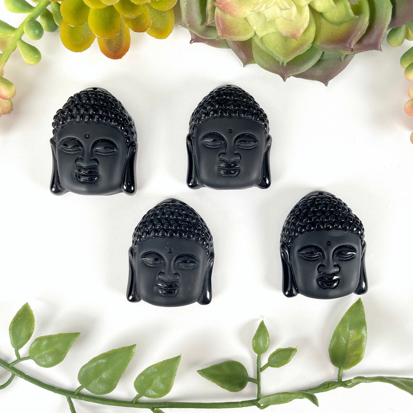 overhead view of four large black onyx buddha head beads on white background with plant decorations for possible variations
