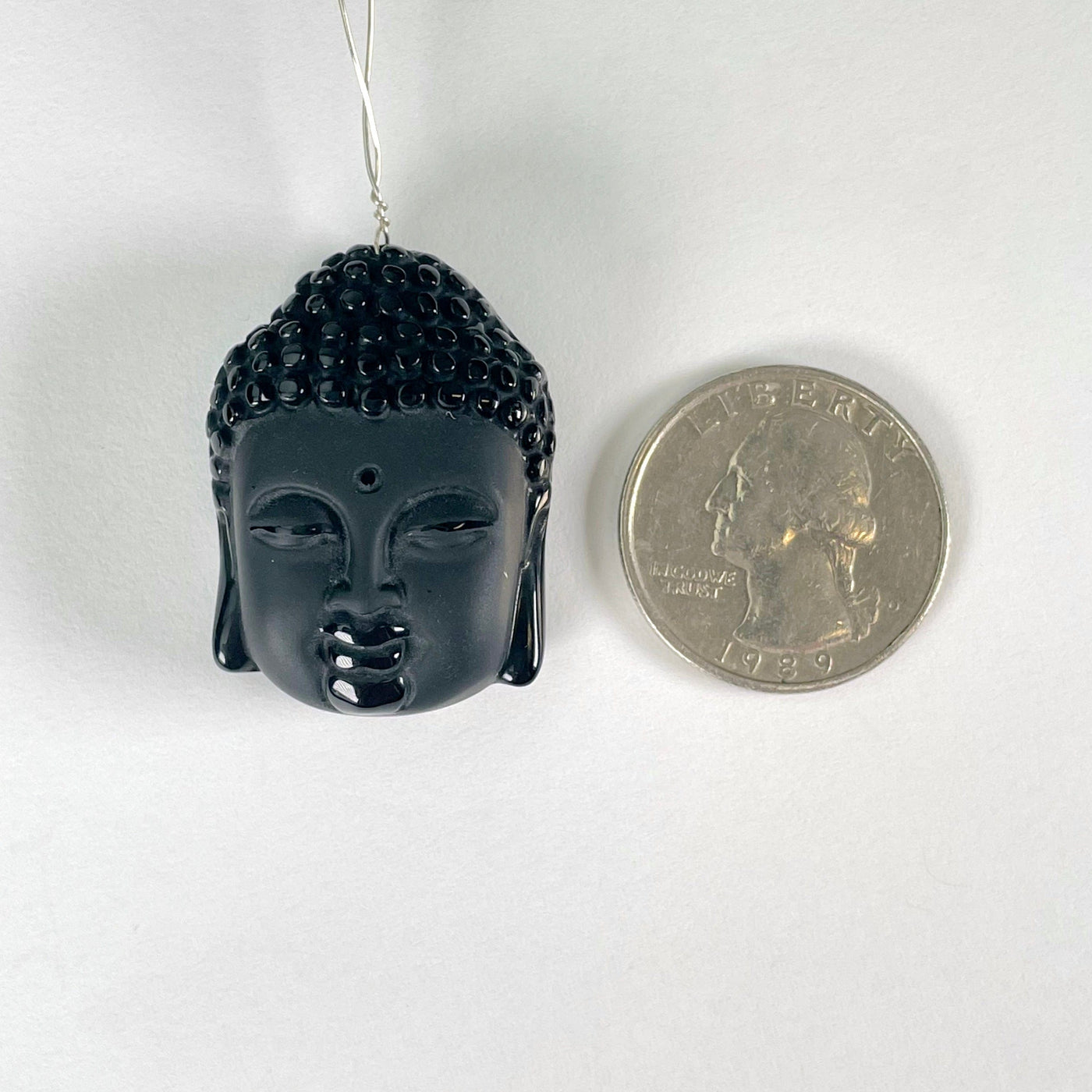 close up of one black onyx buddha head bead on white background with wire going through drilled hole and a quarter for size reference