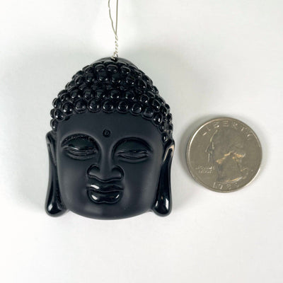 close up of one black onyx buddha head bead with wire running through the drilled hole and a quarter next to it for size reference