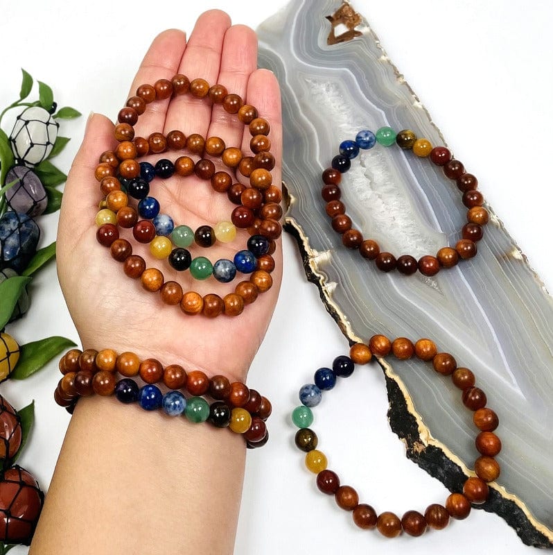 multiple chakra bead bracelets with sandalwood in hand for size reference  