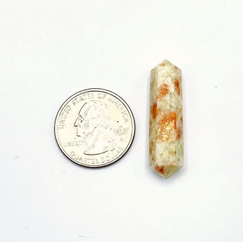 single sunstone double terminated pencil point next to a quarter for size reference on a white background. 