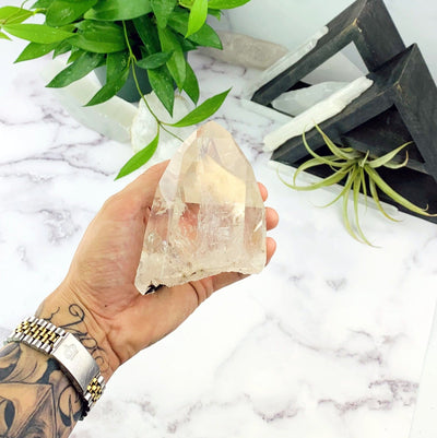 hand holding up Crystal Quartz semi polished point with decorations in the background