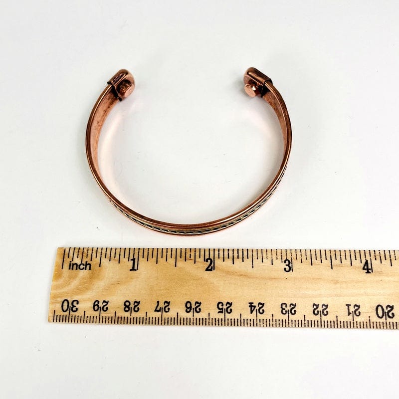 copper bracelet next to a ruler for size reference 