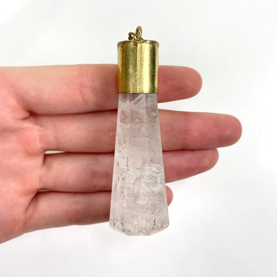 close up of crystal quartz pendant in hand over white background for size reference and details