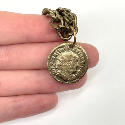 close up of gold coin pendant in hand on white background for size reference and details