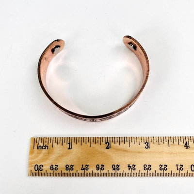 copper engraved bracelet next to a ruler for size reference 