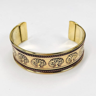 brass bracelet decorated with trees all around and copper accent on the top and bottom of the cuff