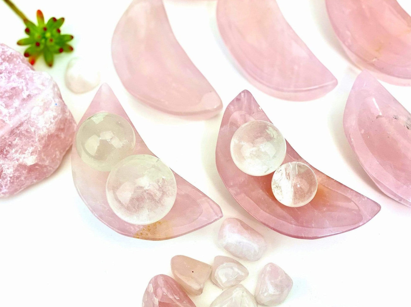 close up of two rose quartz moon bowls with spheres in them on a table with crystals in them
