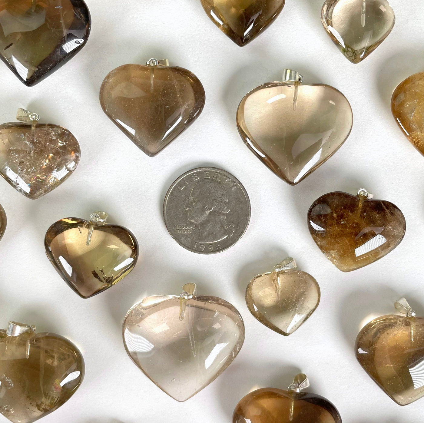 overhead view of many natural citrine heart pendants with quarter on white background for size reference