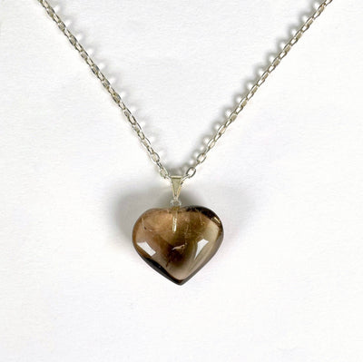 overhead view of one natural citrine heart pendant with chain strung through silver bail on white background