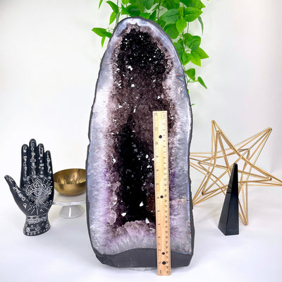 front of amethyst cave geode on display in front of backdrop with vertical ruler for height reference