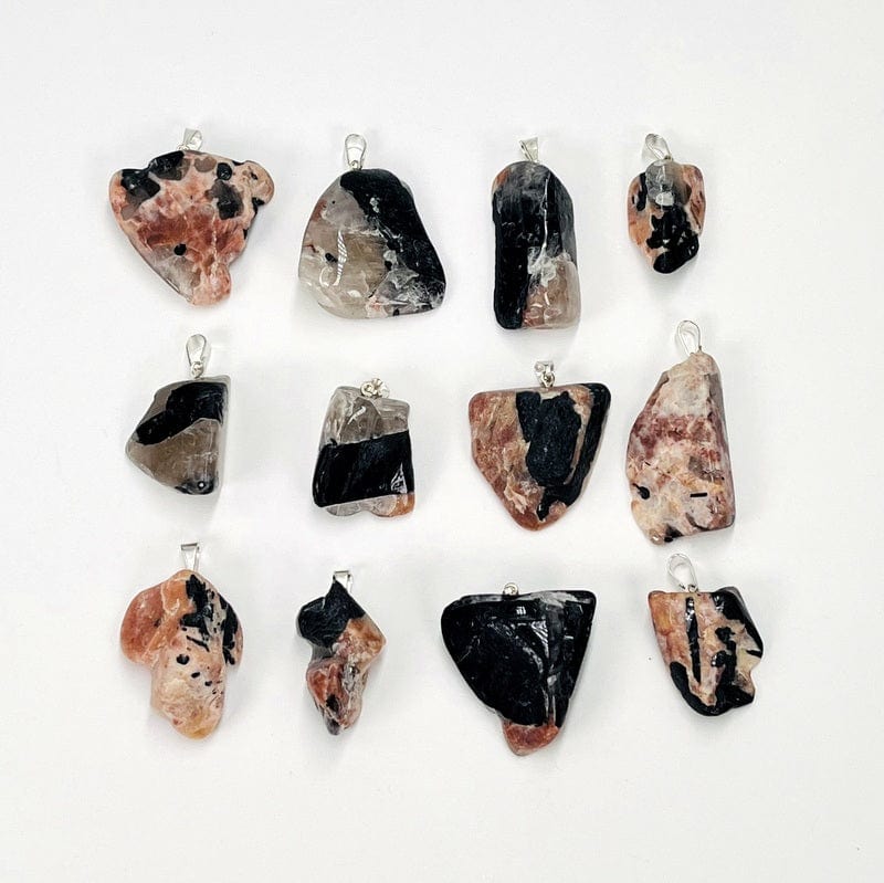 multiple black tourmaline and feldspar pendants displayed next to each other to show the differences in the colors and sizes 