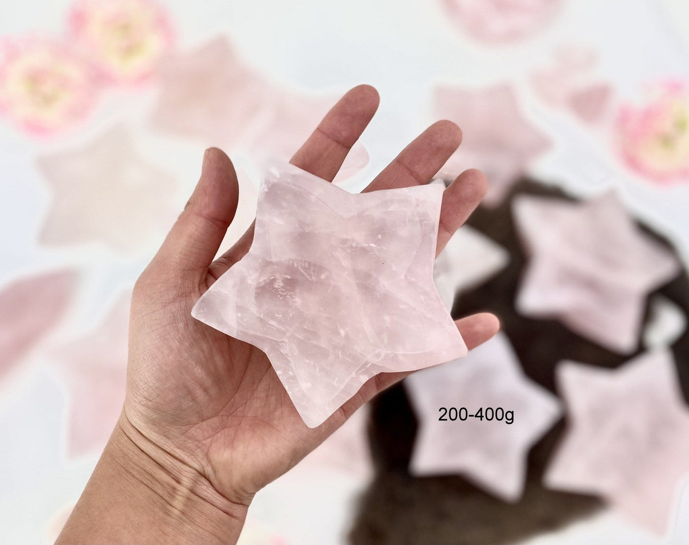 Hand holding up 200-400g Rose Quartz Stone Star Dish with others blurred in the background