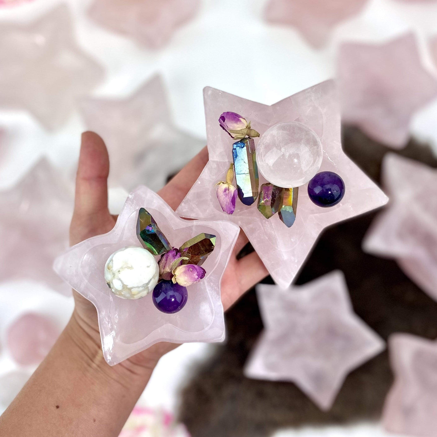 Hand holding up 2 Rose Quartz Stone Star Dishes with crystals inside with others blurred in the background