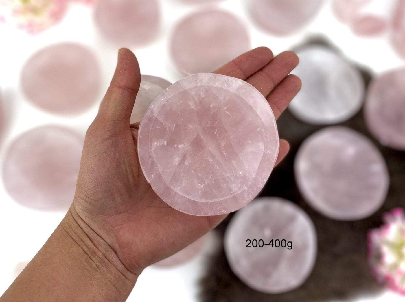 Hand holding up 200-400g Rose Quartz Stone Round Dish with others blurred in the background