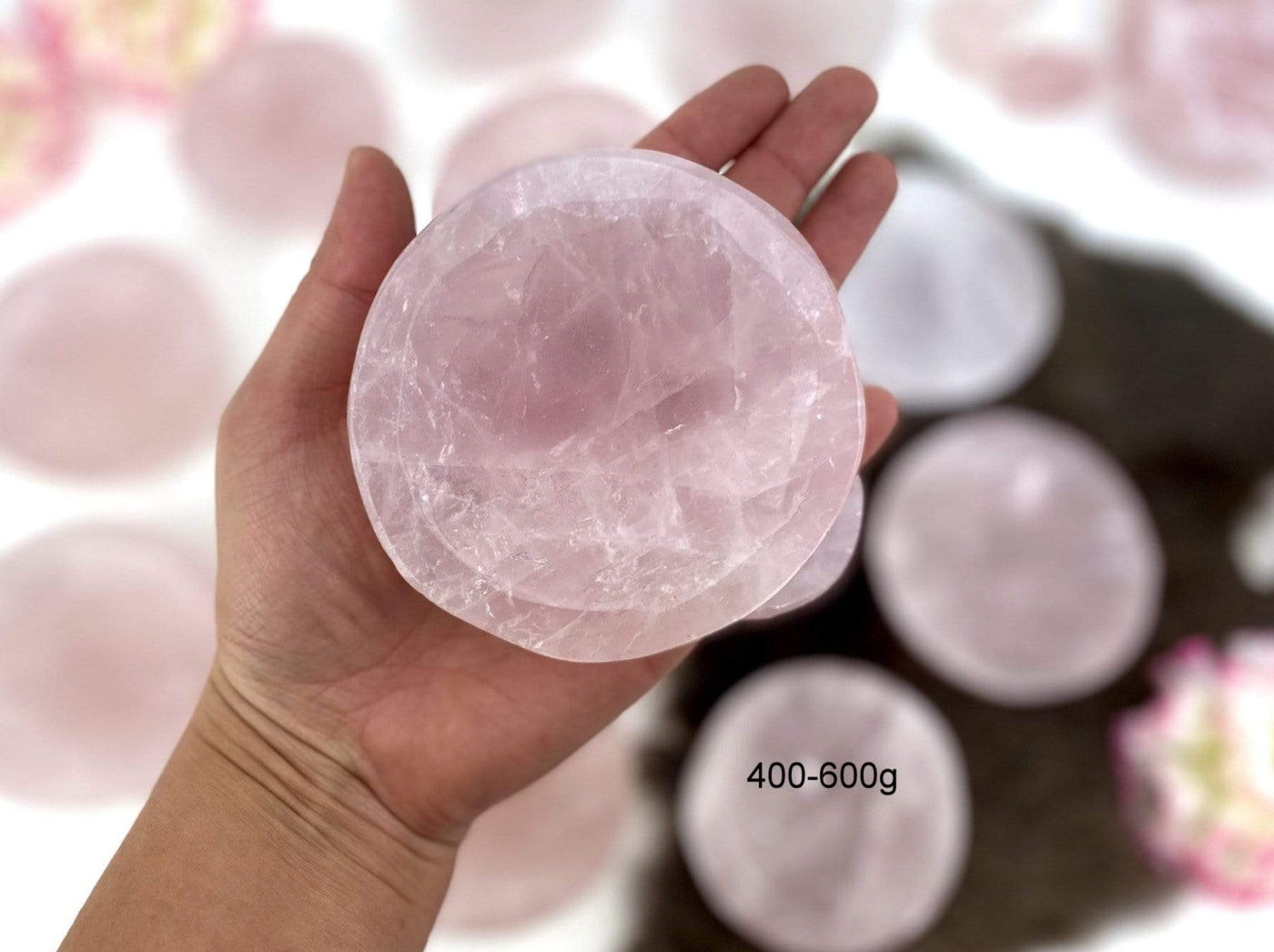 ahnd holding up 400-600g Rose Quartz Stone Round Dish with others blurred in the background