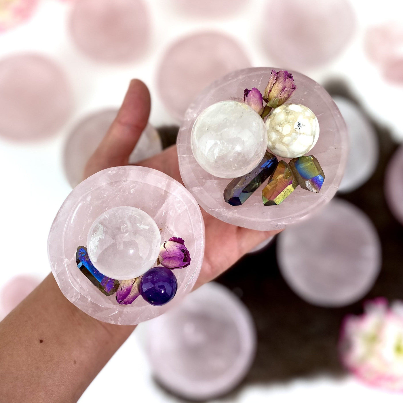 Hand holding up 2 Rose Quartz Stone Round Dishes with crystals inside with others blurred in the background