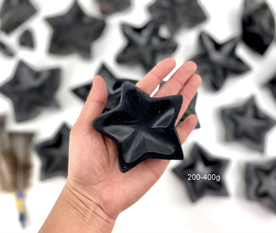 Black Obsidian Stone Star Dish in a hand for size reference of 200-400g size, with others in background