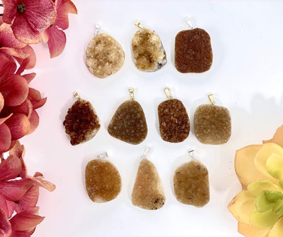 10 assorted druzy cluster pendants withgold and silver plated bails on a white background to show how the shades of orange can vary from dark to light.