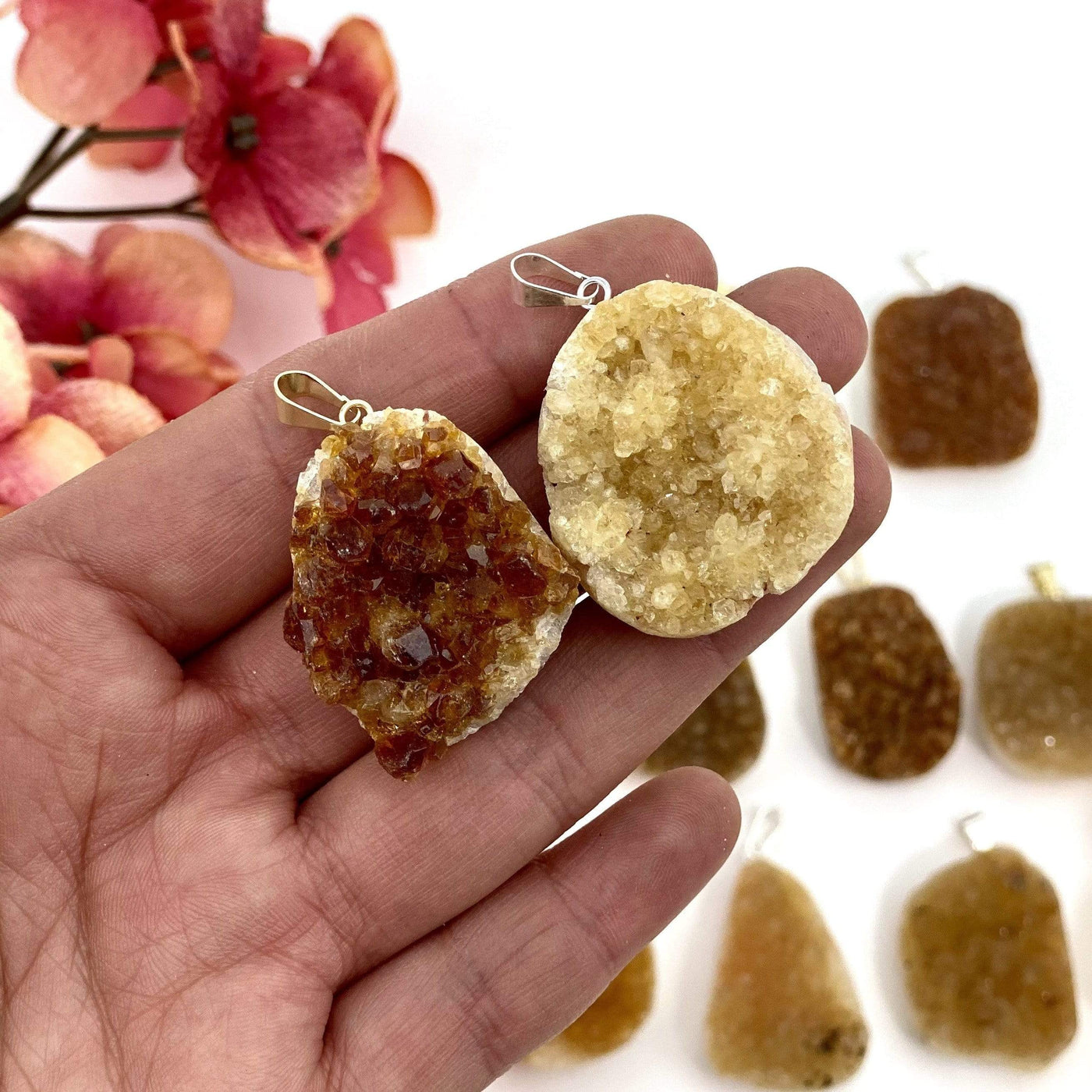 Two citrine cluster pendants in a woman's hand.  They are about three fingers wide.