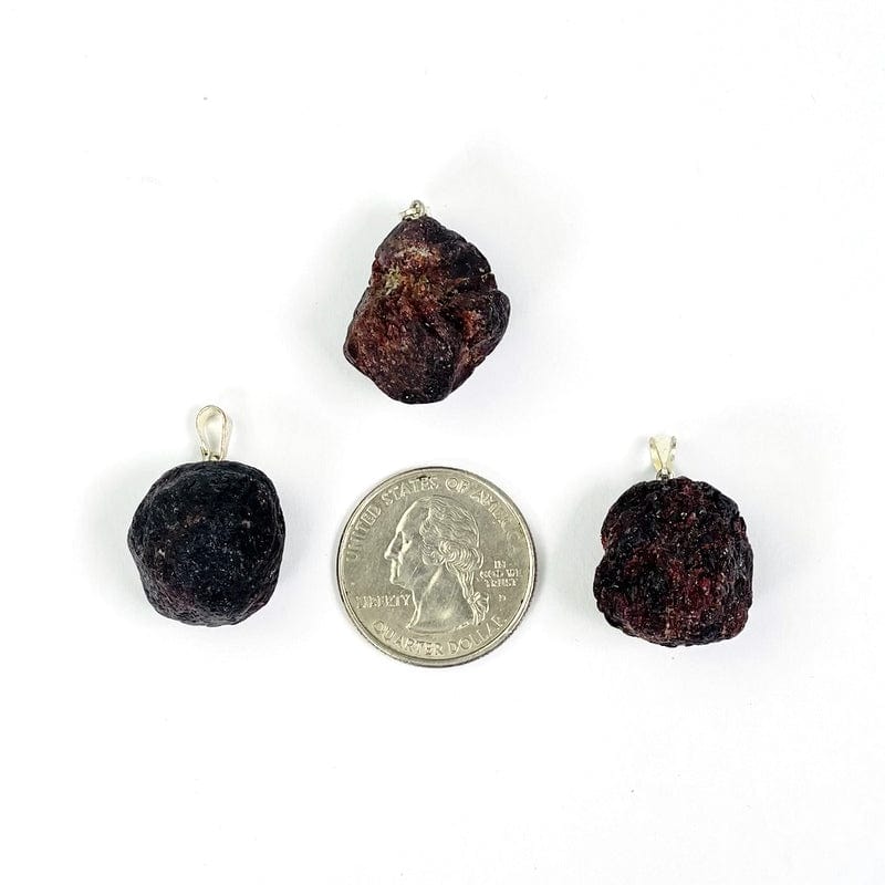raw garnet pendants with silver bail next to a quarter for size reference 