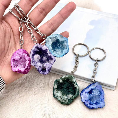 multiple different colored half occo geode silver toned keychain shown in hand for size reference 