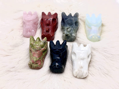 Close Up of 7 Different Dragon Head Mini Statues on White Furry Carpet.