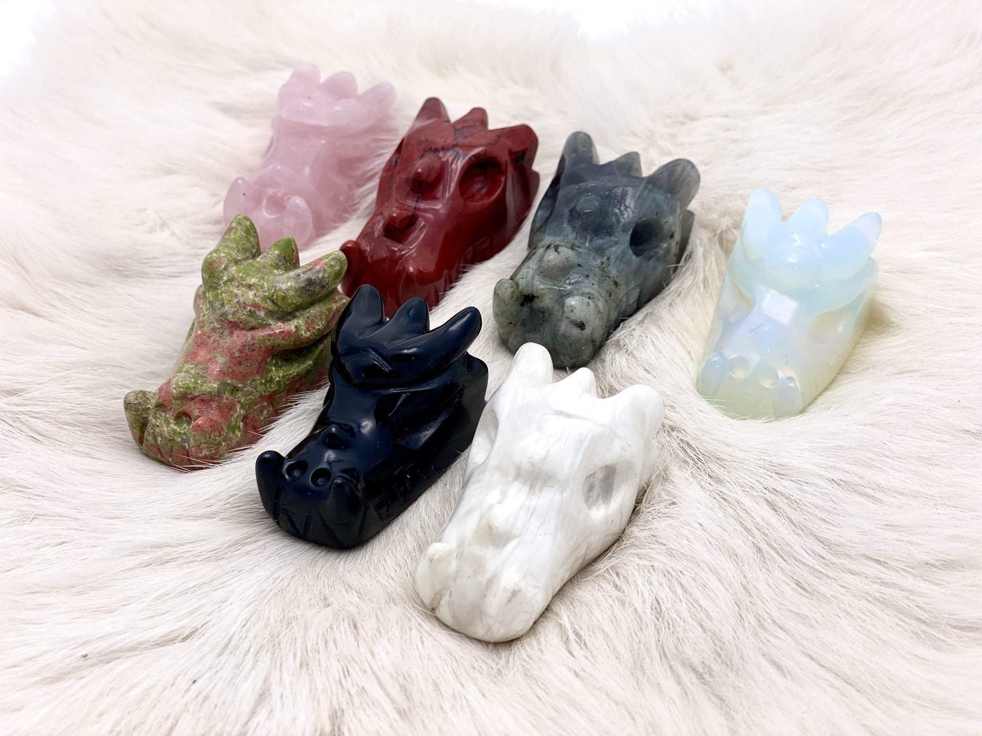 7 Different Dragon Head Mini Statues on White Furry Carpet.