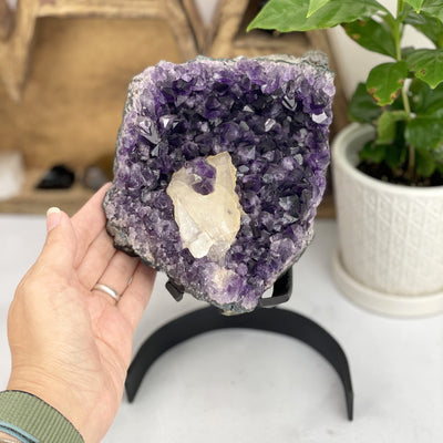 hand next to Amethyst Crystal Cluster with Calcite  with decorations in the background
