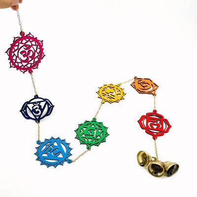 close up of wooden wall hanger with colorful chakra symbols and three attached bells at the bottom