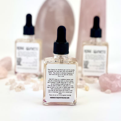 Back of bottle of Rose Quartz Gem Essence with instructions with 2 other bottles blurred in the background with other rose quartz crystals