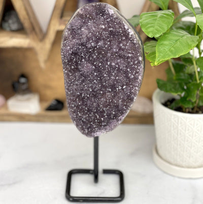 amethyst cluster on a black metal stand shown on a white background.