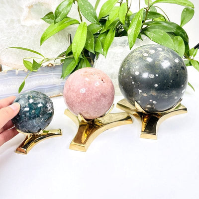 All three sizes of sphere holders with crystal spheres on them and a woman's hand holding the sphere on the smallest holder.