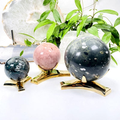 All three sizes of sphere stands with the middle tubing taken out so they lay lower.  They are shown with assorted crystal spheres on them on a white background.