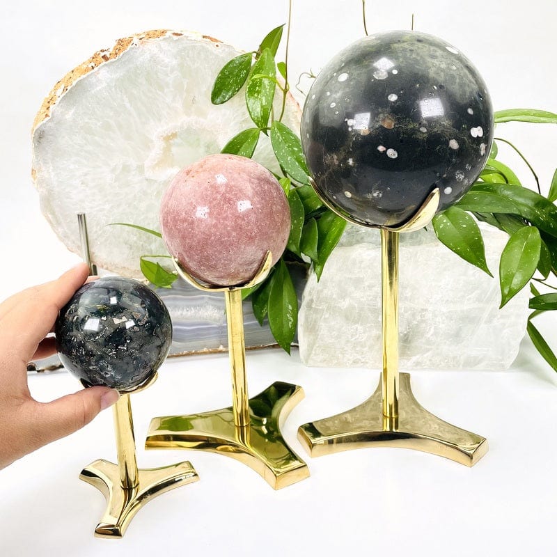 All three size of sphere stands with spheres on them for display and a woman's hand holding the sphere on the small stand.