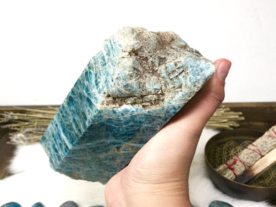 hand holding up Blue Apatite Polished Point Chunk with decorations in the background