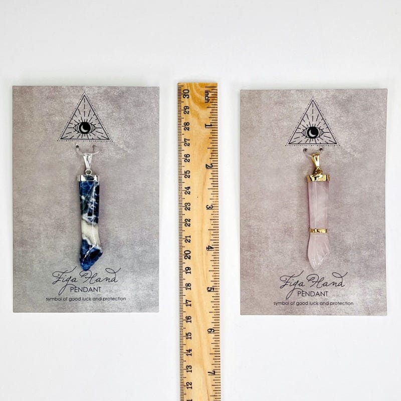 pendant and information card next to a ruler for size reference 