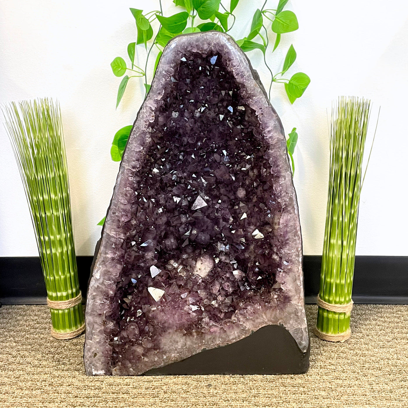 front of amethyst cave geode on display in front of plant décor 