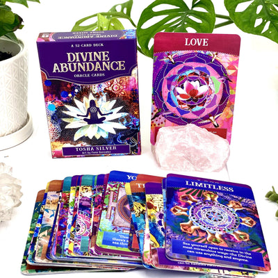 Divine Abundance Oracle Card Deck With 52 Card Lying Down in Top of Each Other on White Background.