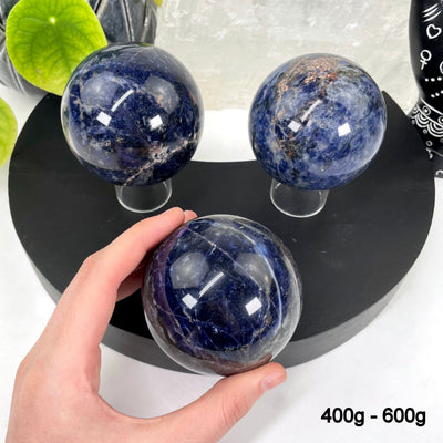 three 400g - 600g sodalite polished spheres on display for possible variations with one in hand for size reference